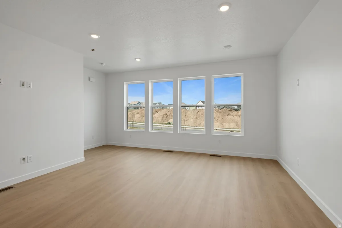 Spacious living area featuring light wood-finish flooring, recessed lighting, and multiple windows