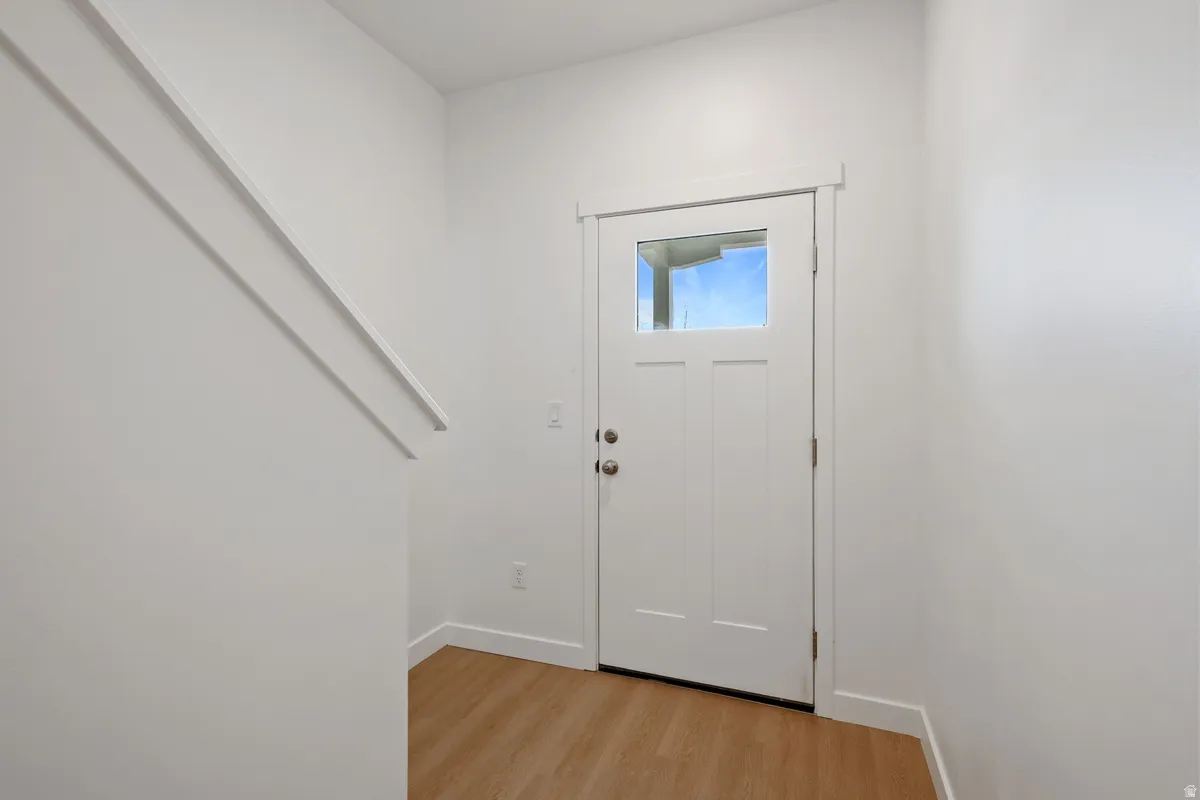 Entryway featuring a Craftsman-style door with clear glass, light wood-finish flooring, white baseboards, and a white interior staircase wall