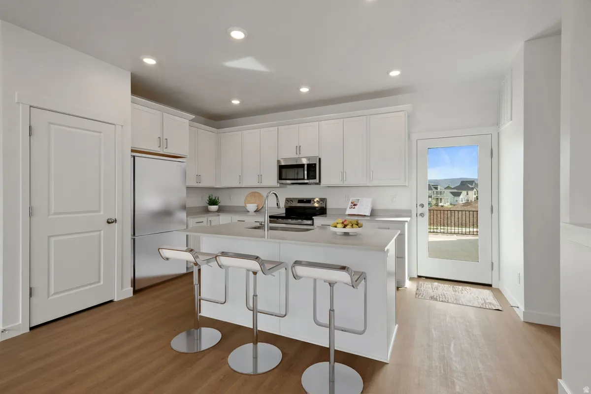Modern kitchen featuring white cabinetry, stainless steel appliances, a center island with bar seating, wood-finish flooring, and recessed lighting