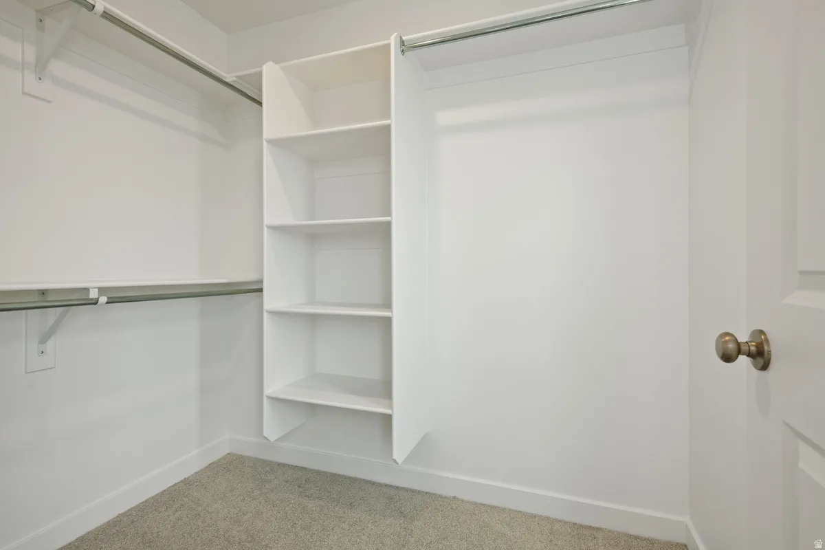 Walk-in closet featuring white built-in shelving, two levels of hanging rods, and light-colored carpet flooring