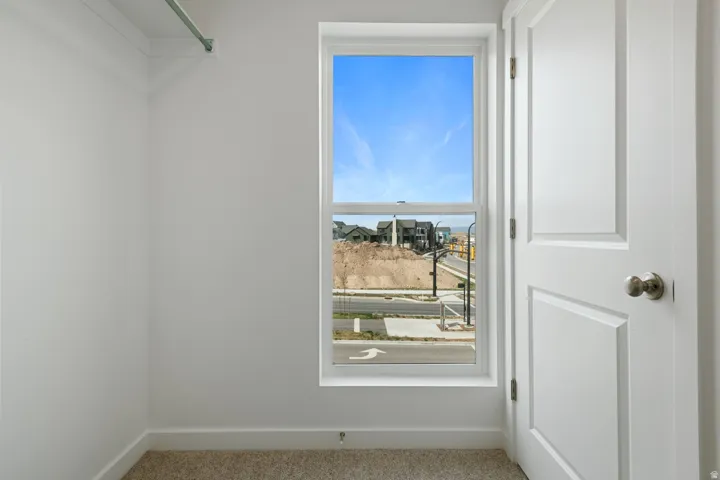 Compact interior space featuring a single window, a white paneled door with brushed nickel hardware, light-colored carpeting, and a clothing rod