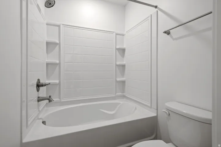 White bathtub with an integrated shower, featuring a tiled surround and built-in shelving