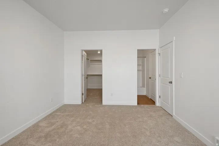 Spacious room featuring neutral carpeting and white painted walls, with two separate doorways