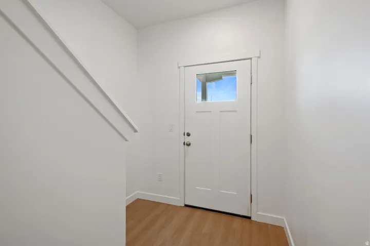 Entryway featuring a Craftsman-style door with clear glass, light wood-finish flooring, white baseboards, and a white interior staircase wall