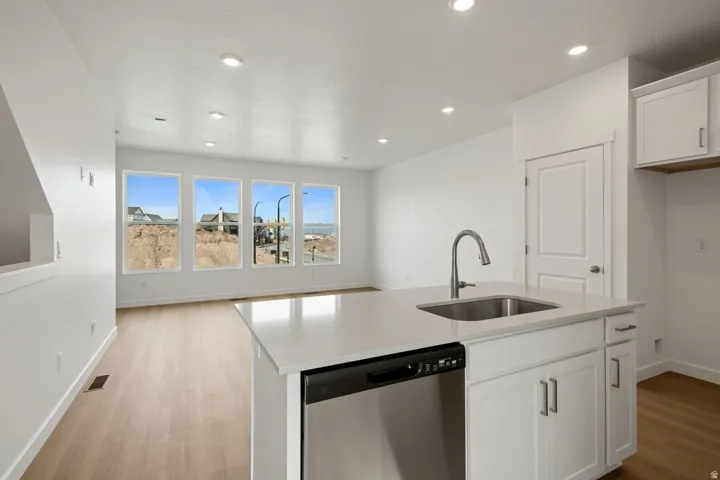 Open concept kitchen and living area featuring an island with a stainless steel sink, a dishwasher, white cabinetry, light wood-finish flooring, and recessed lighting