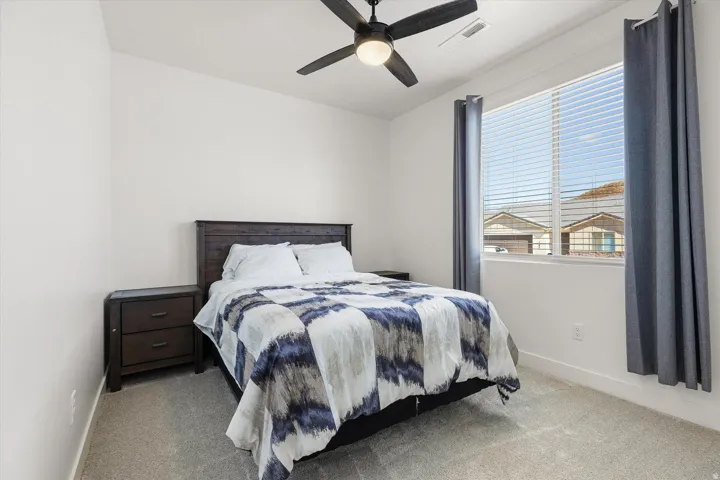 Bedroom featuring a ceiling fan with integrated lighting, a large window with horizontal blinds, neutral-toned walls, and carpet flooring