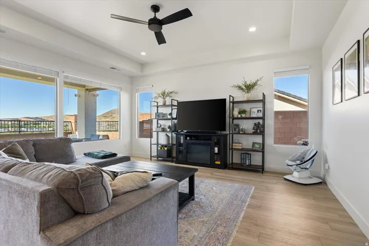 Living area featuring large windows, wood-finish flooring, a ceiling fan, recessed lighting, and a tray ceiling