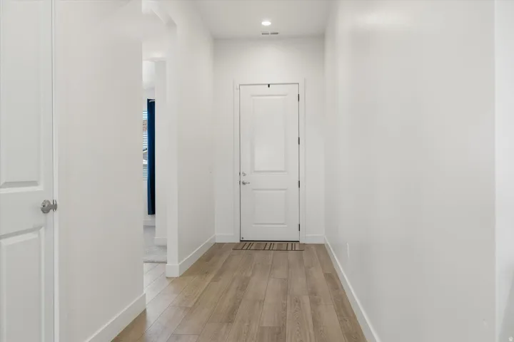 Bright white hallway featuring wood-finish flooring, recessed lighting, and a paneled entry door
