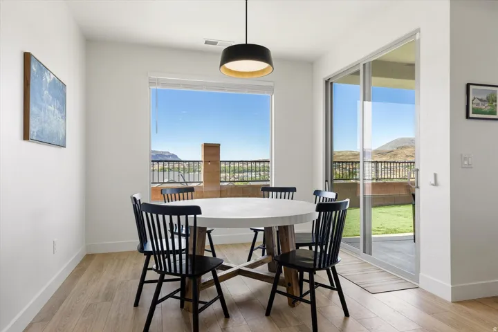 Bright dining area featuring wood-finish flooring, a contemporary pendant light fixture, a large window, and sliding glass doors leading to an exterior balcony with mountain scenery
