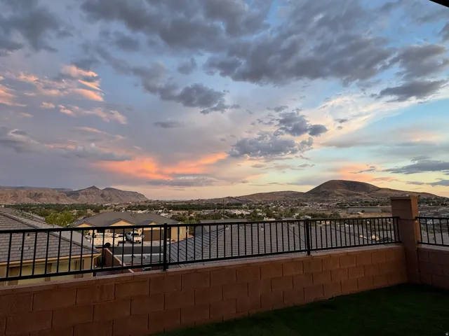 Expansive outdoor space featuring a retaining wall with a black metal railing, overlooking distant mountains and residential rooftops