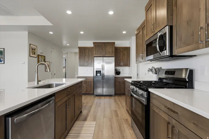 Modern kitchen featuring wood-finish cabinetry, stainless steel appliances, white countertops, and recessed lighting