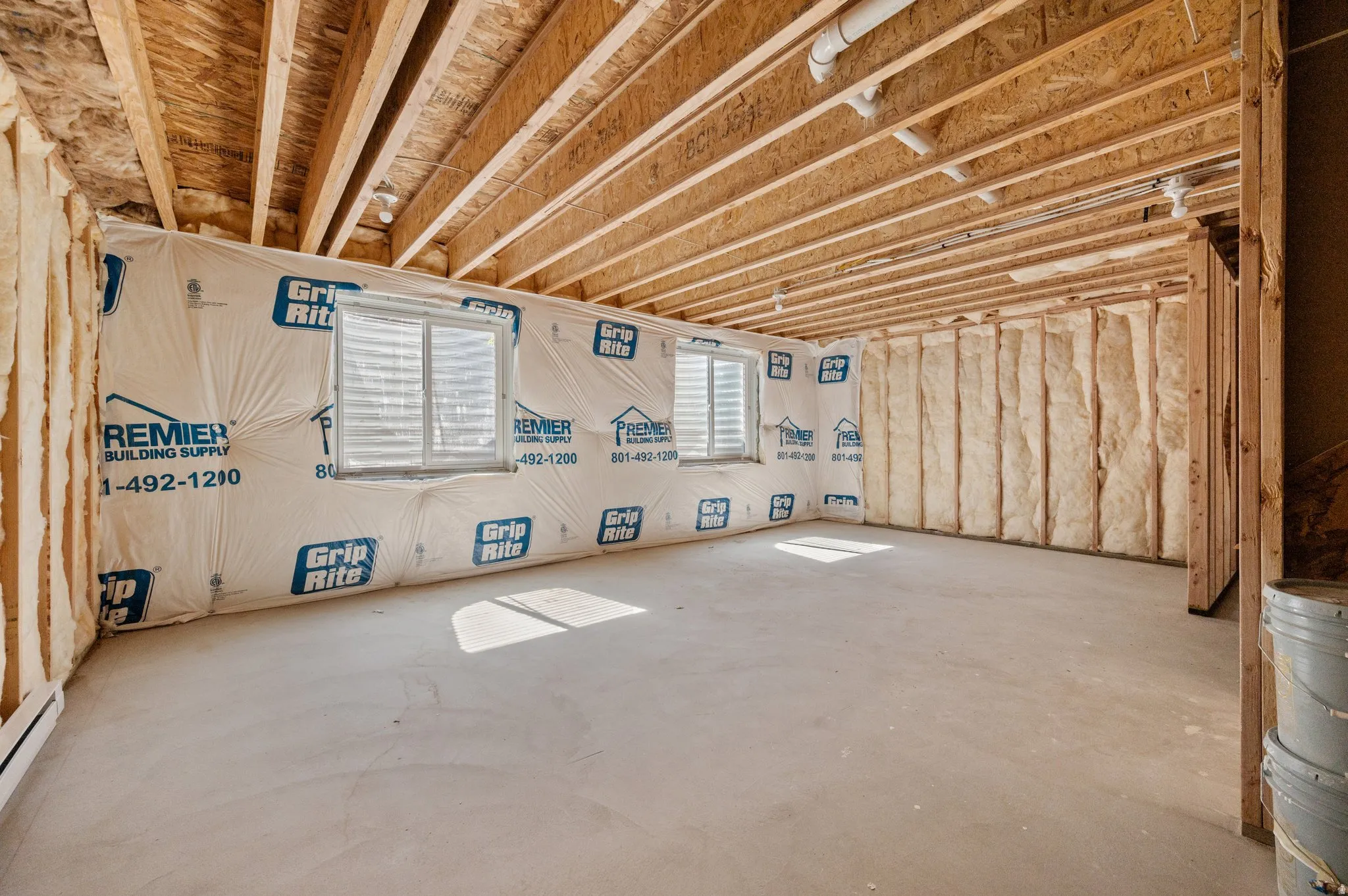 Unfinished basement featuring exposed wood joists, framed walls, two windows, and concrete flooring