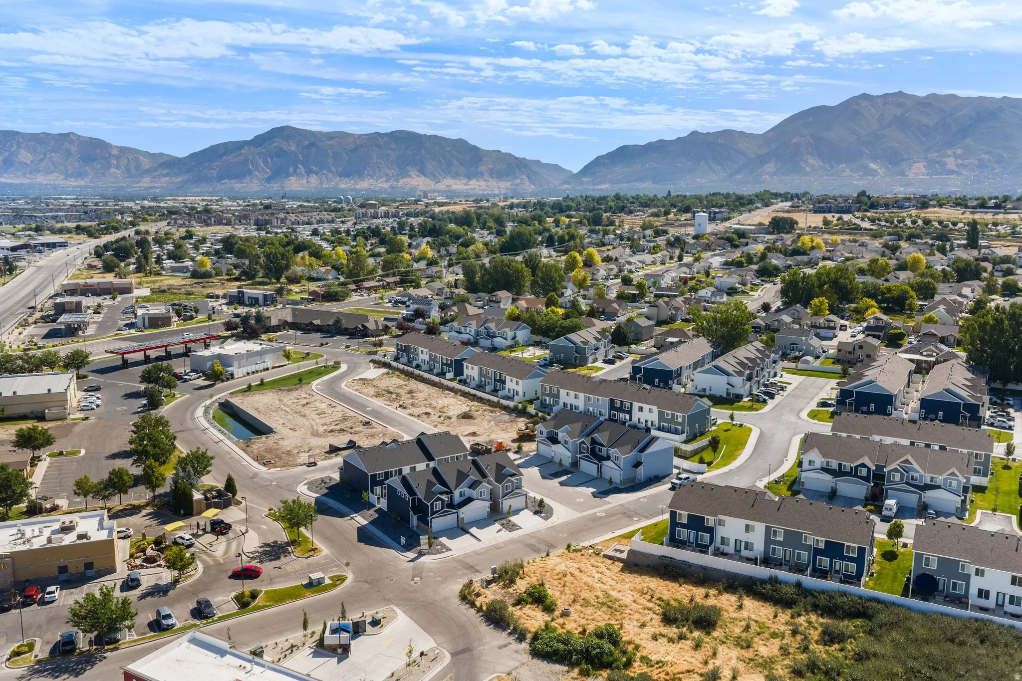 Aerial perspective showcasing a residential development with new construction homes, surrounding commercial properties, and a prominent mountain range backdrop