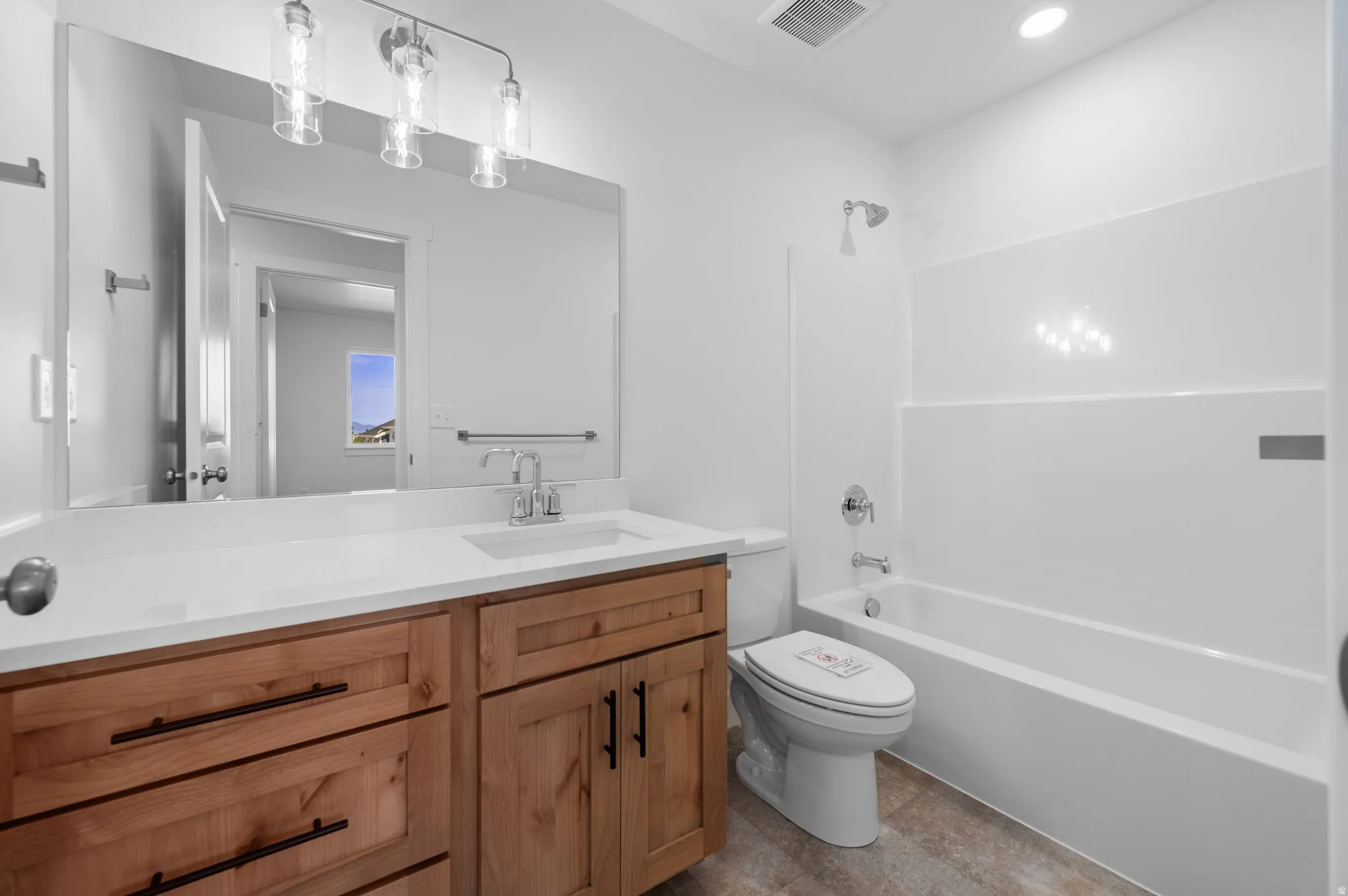 Bathroom featuring a light wood-finish vanity with a white countertop and undermount sink, a large mirror, a three-light vanity fixture, and a white tub-shower combination