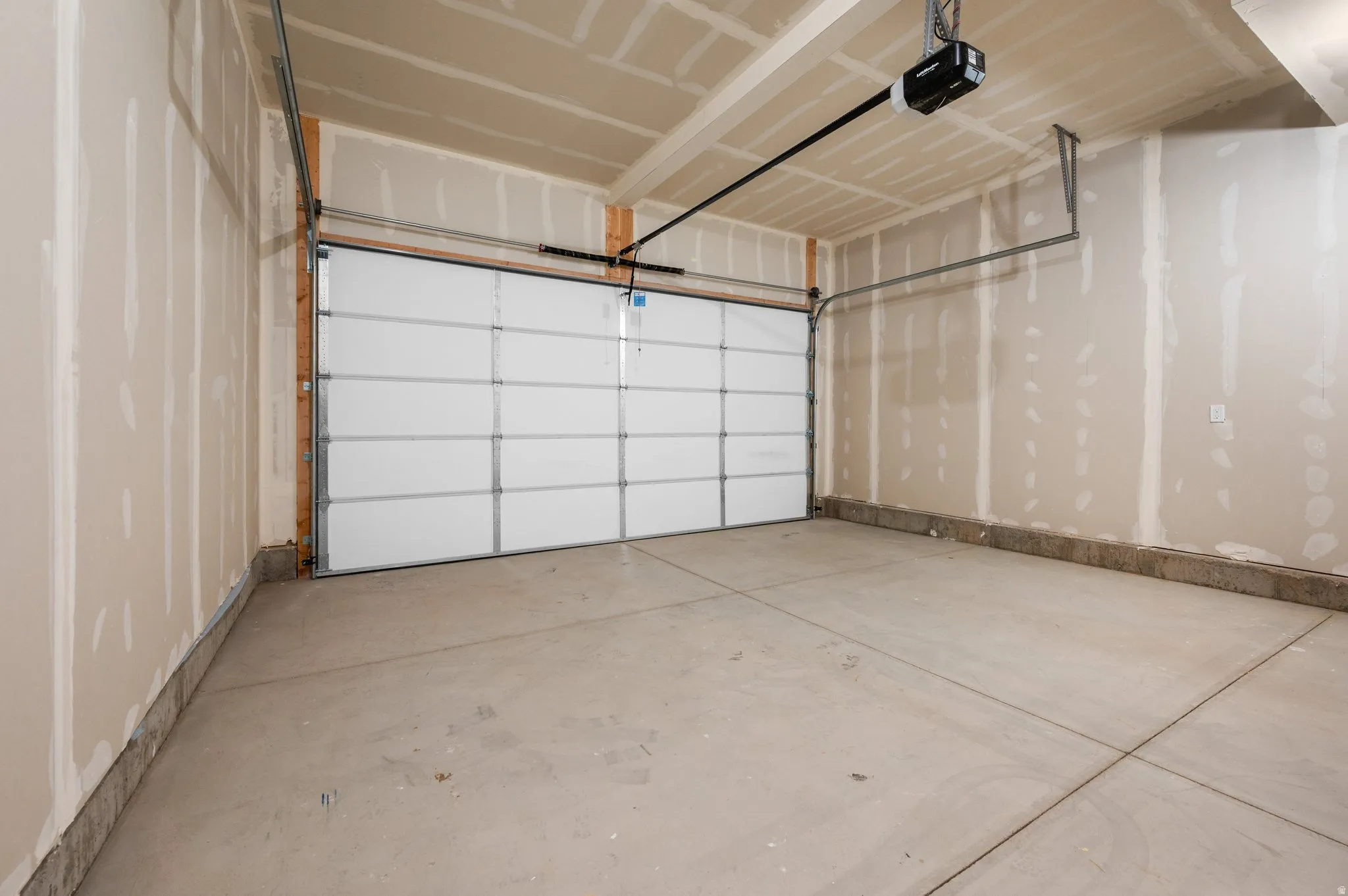 Spacious garage featuring a concrete floor, an overhead garage door, an automatic opener, and unfinished drywall