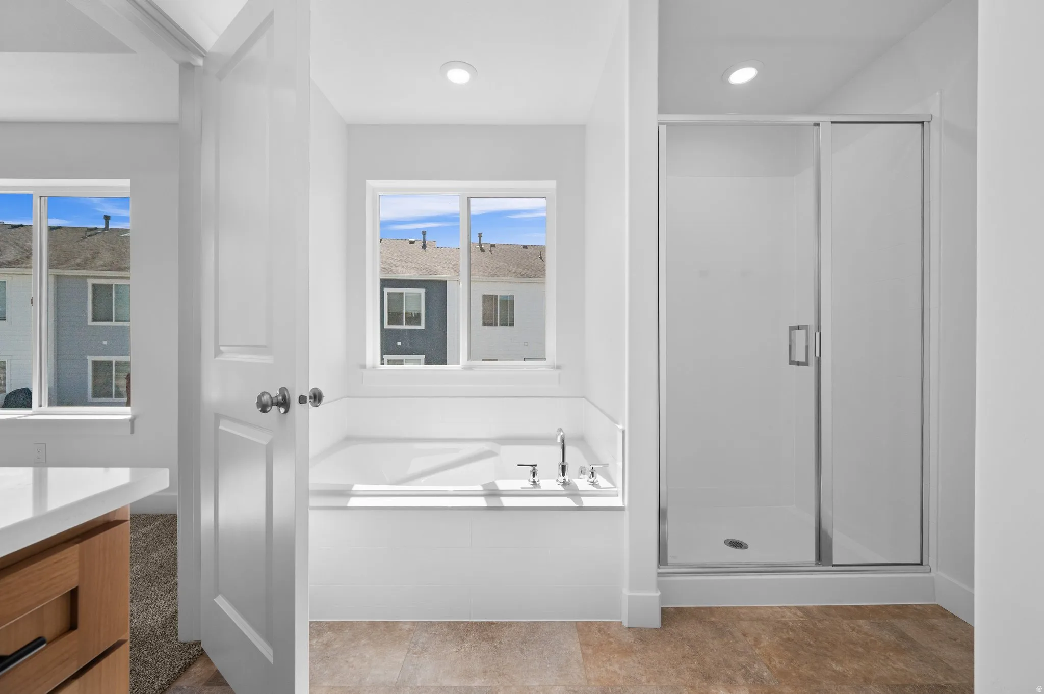 Contemporary bathroom featuring a built-in soaking tub with chrome fixtures, a separate glass-enclosed shower, light wood-finish flooring, recessed lighting, and a window providing natural illumination