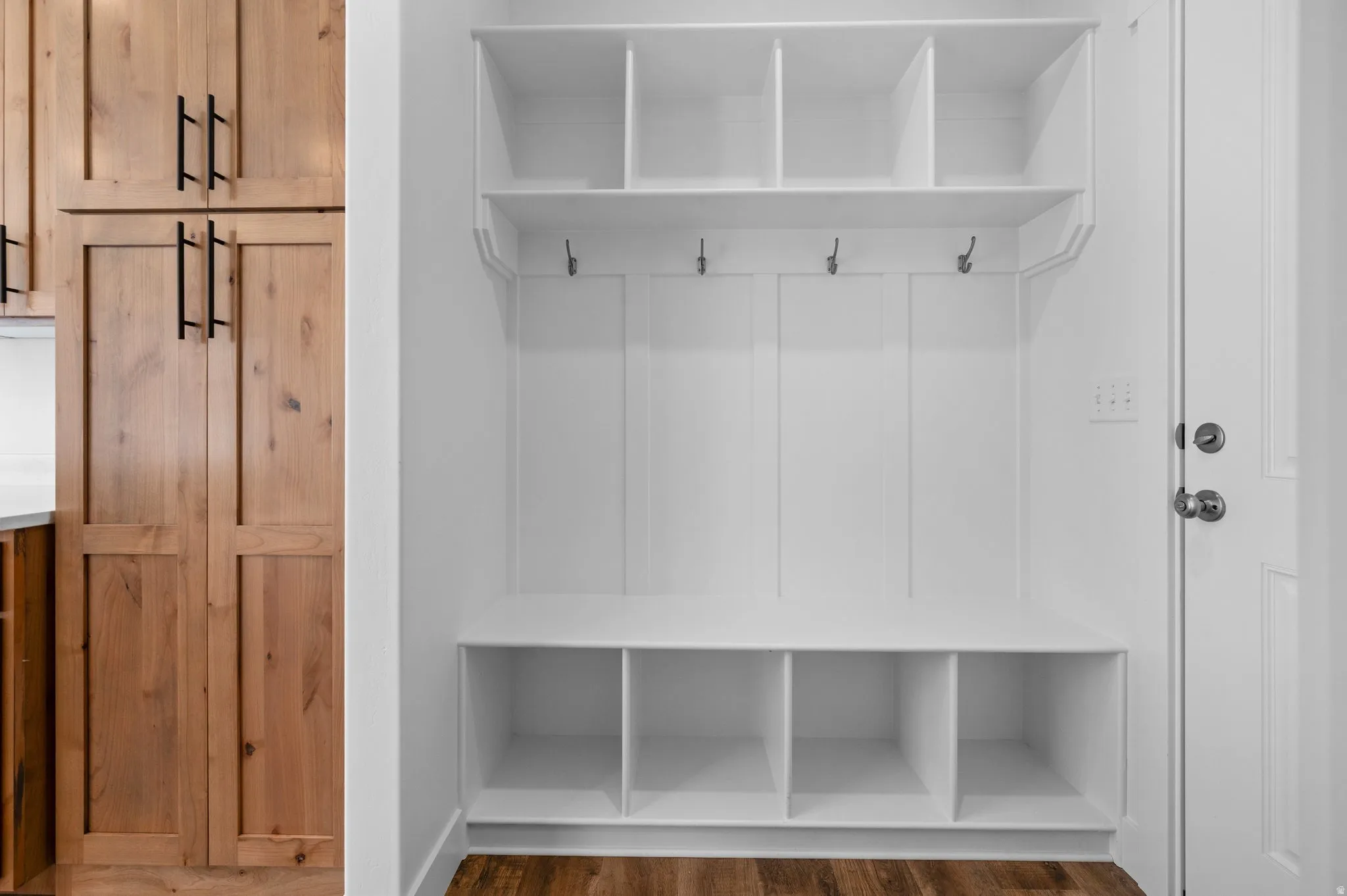 Built-in white storage bench with open cubbies, upper shelving, and coat hooks
