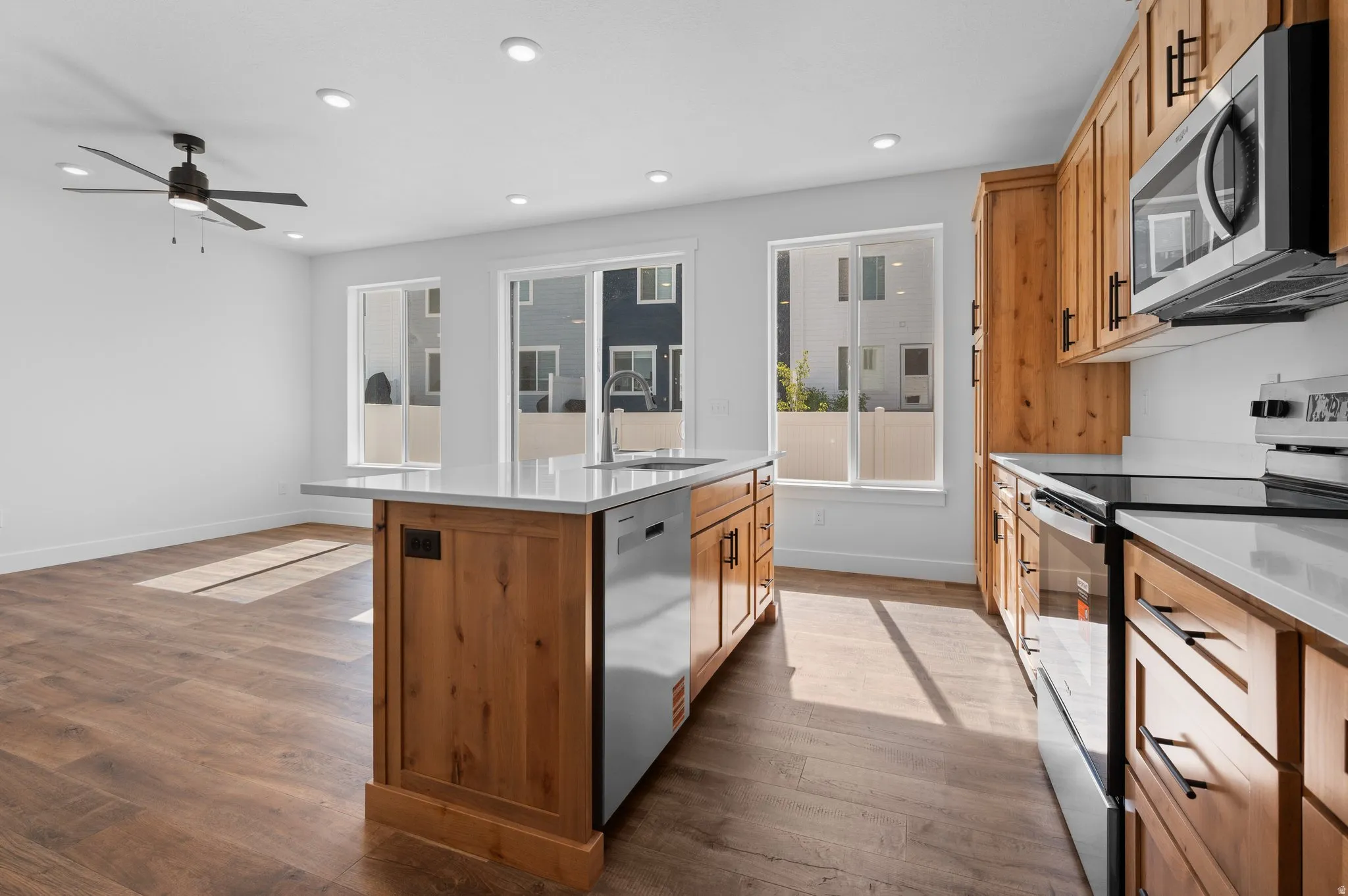 Modern kitchen featuring wood-finish cabinetry, stainless steel appliances, and a central island with a sink and white countertop