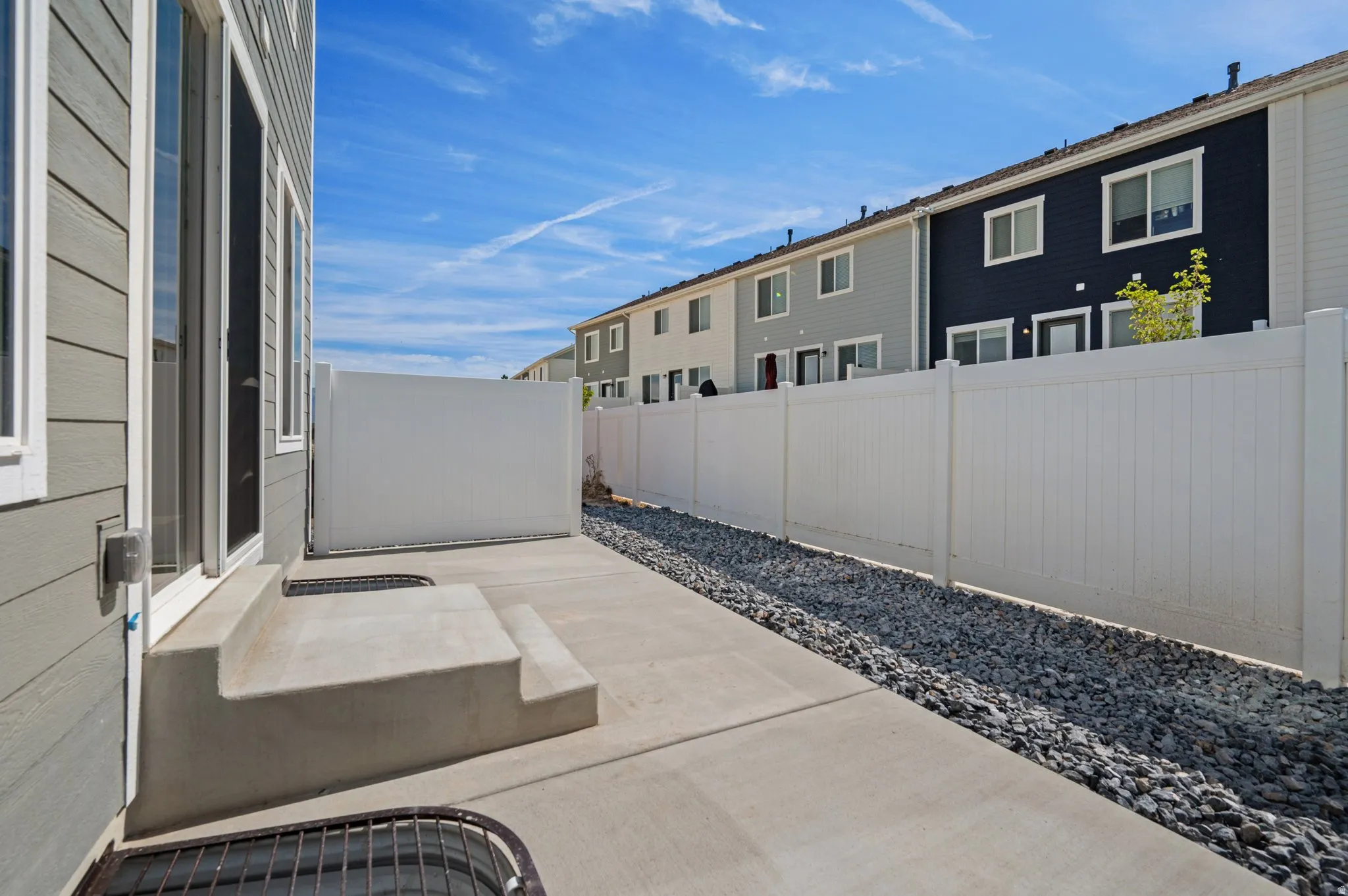 Concrete patio with steps from the rear entrance, featuring an adjacent privacy fence and decorative gravel landscaping