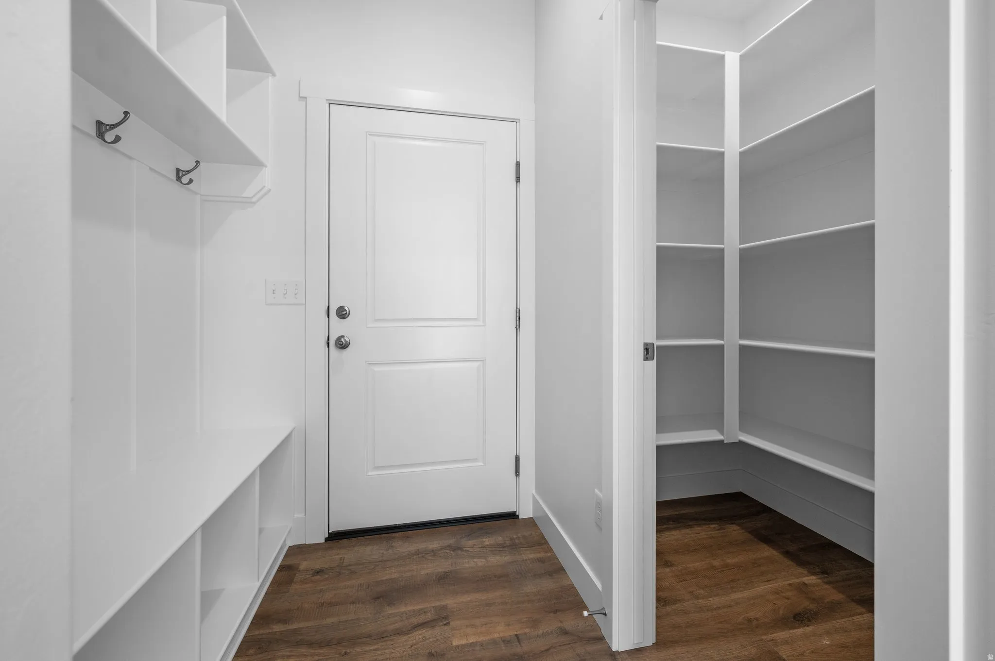 Mudroom and pantry area featuring built-in shelving, coat hooks, wood-finish flooring, and white paneled doors