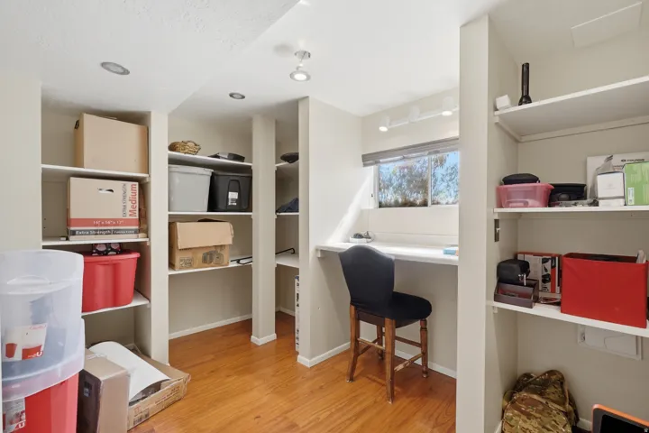 Built-in desk area with a window, surrounded by multiple open shelving units and recessed lighting