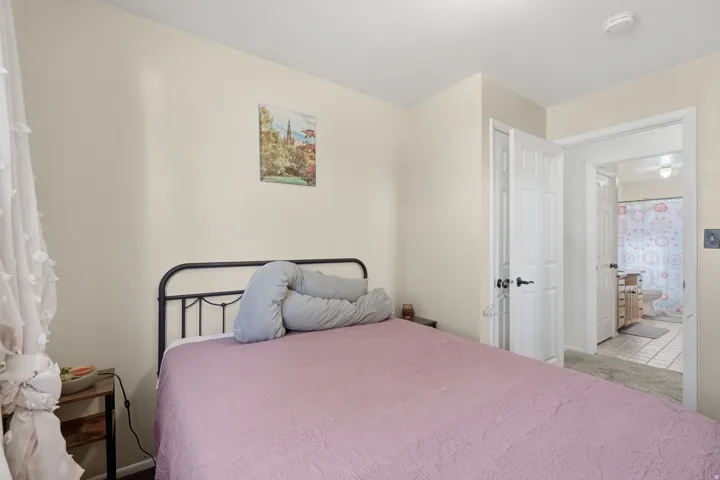 Bedroom featuring light-colored walls, carpet flooring, a white paneled door, and an open doorway revealing a bathroom with tile flooring and a vanity
