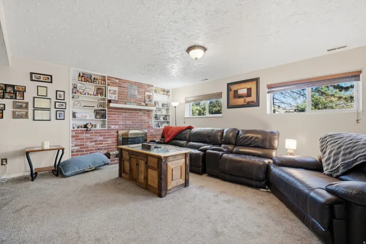 Living area featuring a brick accent wall with an integrated fireplace and built-in shelving, complemented by neutral carpeting and recessed windows