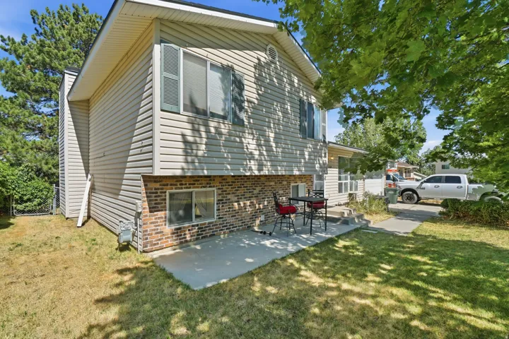 Exterior featuring light-colored siding and brick accents, a concrete patio, and a grassy lawn