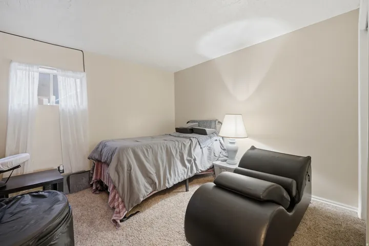 Carpeted room featuring a window with white sheers, light beige walls, and a white ceiling