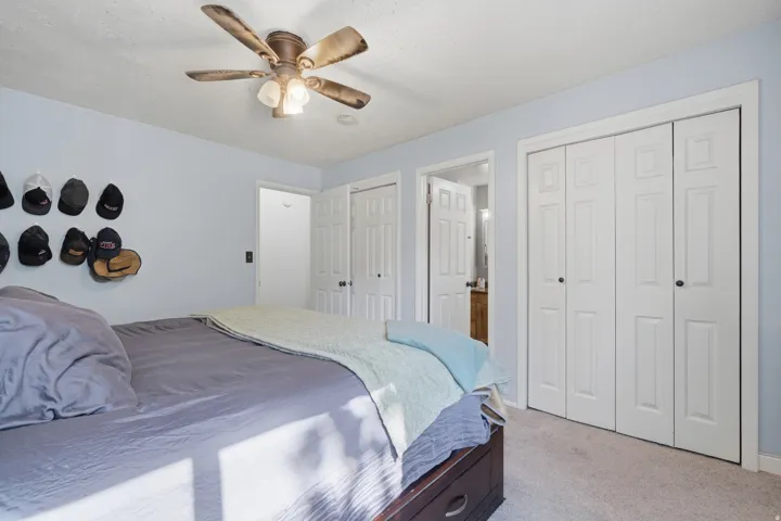 Carpeted room featuring a ceiling fan with integrated lighting, multiple white paneled bifold closet doors, and light blue wall tones