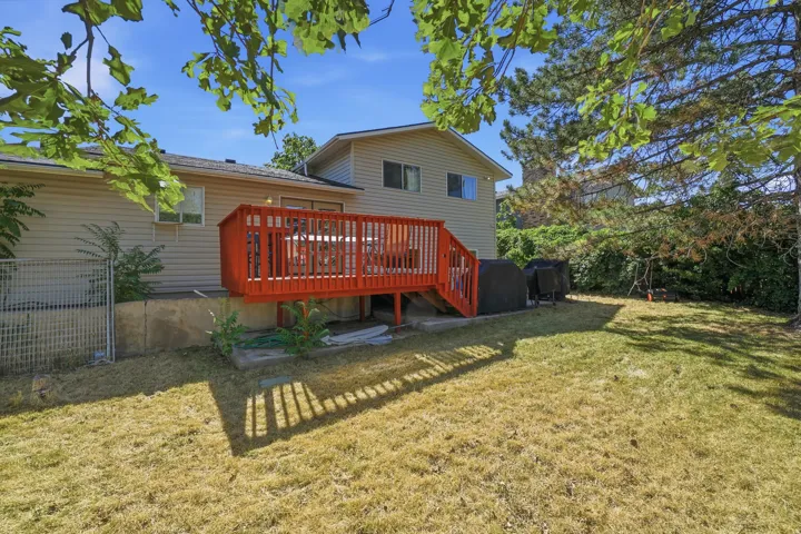 Expansive backyard featuring a red wood deck, a partial fence, and mature trees providing natural shade