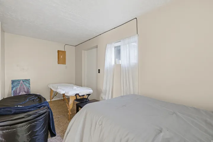 Room featuring a window with sheer white curtains, light-toned walls, a textured ceiling, and carpet flooring