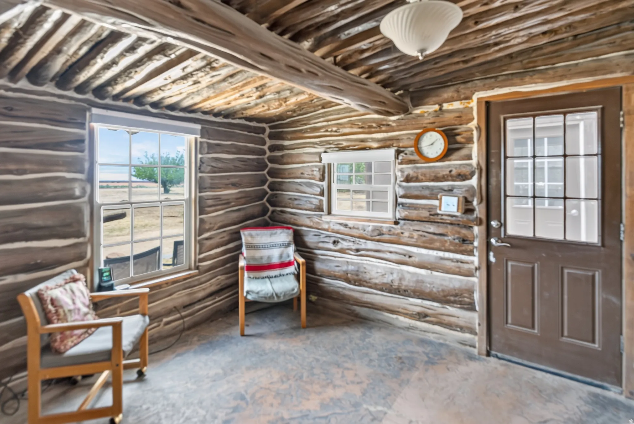 Log cabin interior featuring exposed log walls, a beamed ceiling, a multi-pane window, and a door with divided lites