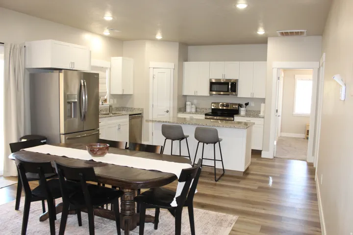 Open-concept kitchen and dining area featuring wood-finish flooring, white cabinetry, stainless steel appliances, granite countertops, and recessed lighting