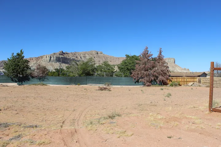 Expansive lot featuring a distant mountain backdrop, existing perimeter fencing, and mature trees on the property line