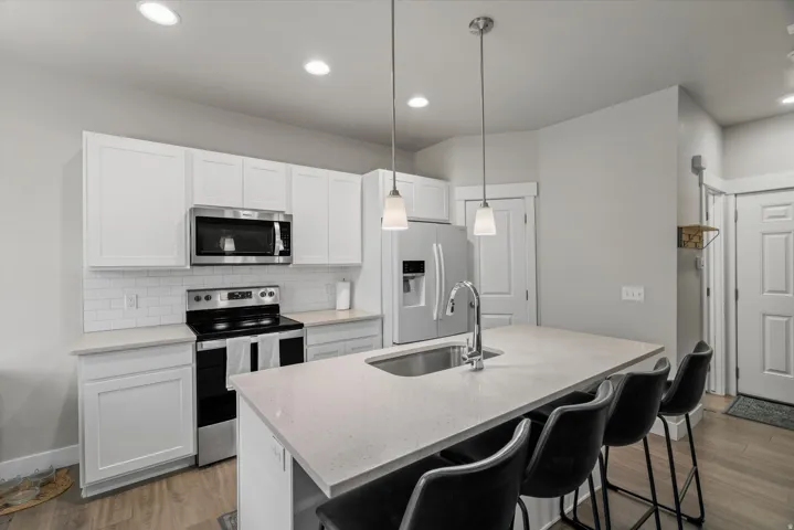 Modern kitchen featuring white shaker cabinetry, stainless steel appliances, a subway tile backsplash, and a large island with a stainless steel sink and pendant lighting
