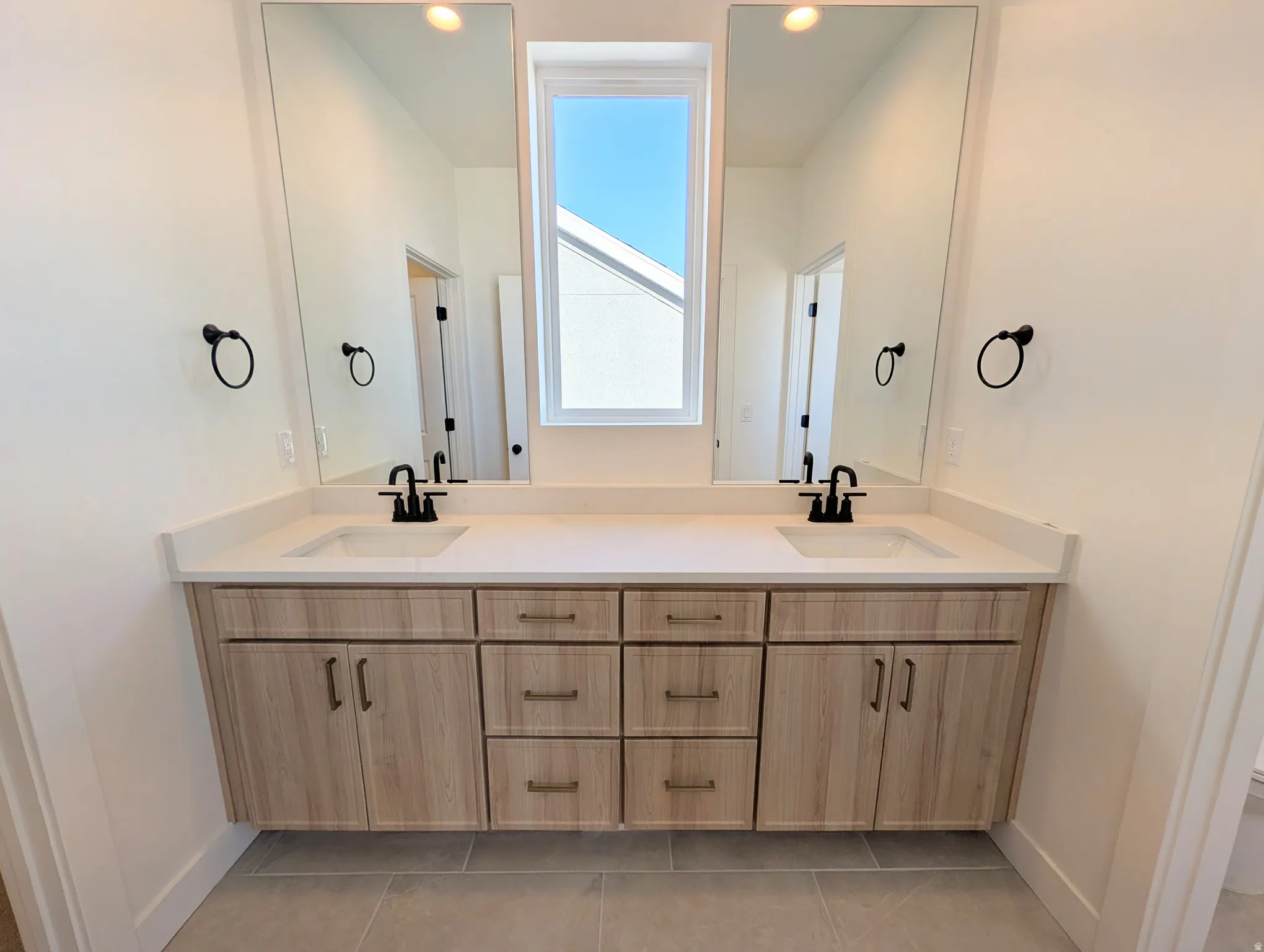Dual floating vanities with wood-finish cabinetry, light-toned countertops, and matte black fixtures