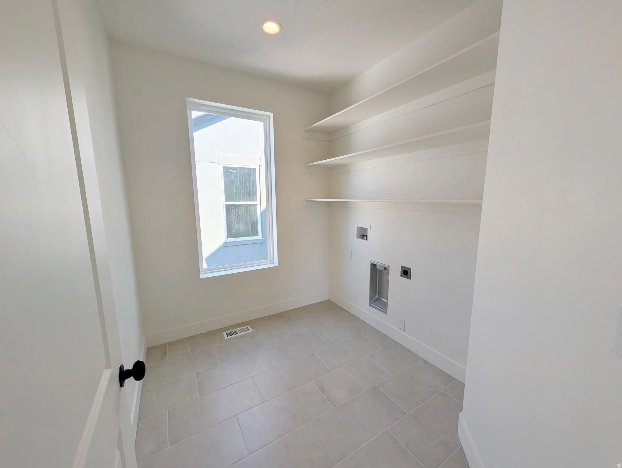 Built-in shelving, recessed lighting, rectangular window, tile flooring, and a door with black hardware