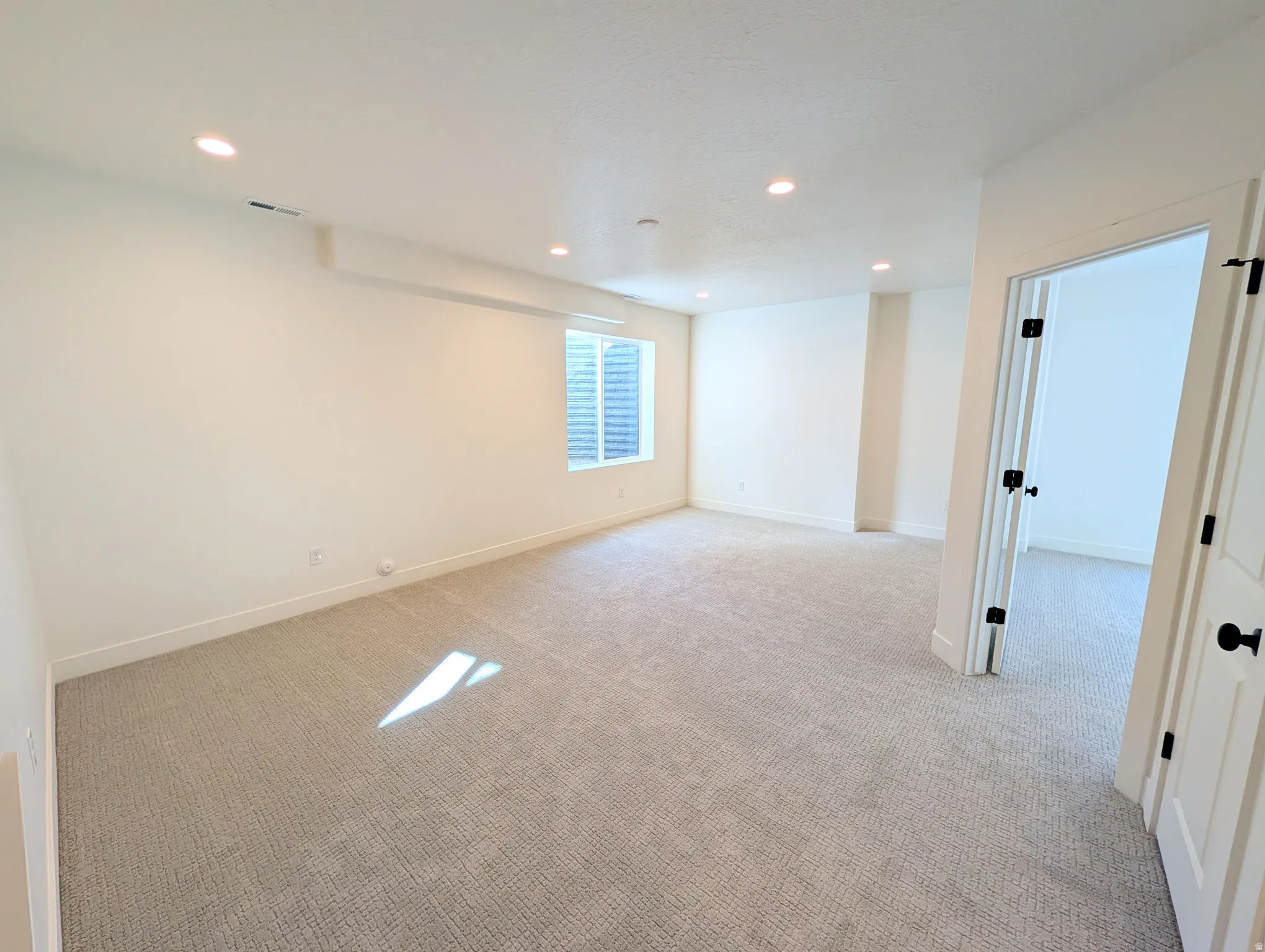 Spacious room with recessed lighting, light-toned carpeting, and white interior doors with black hardware