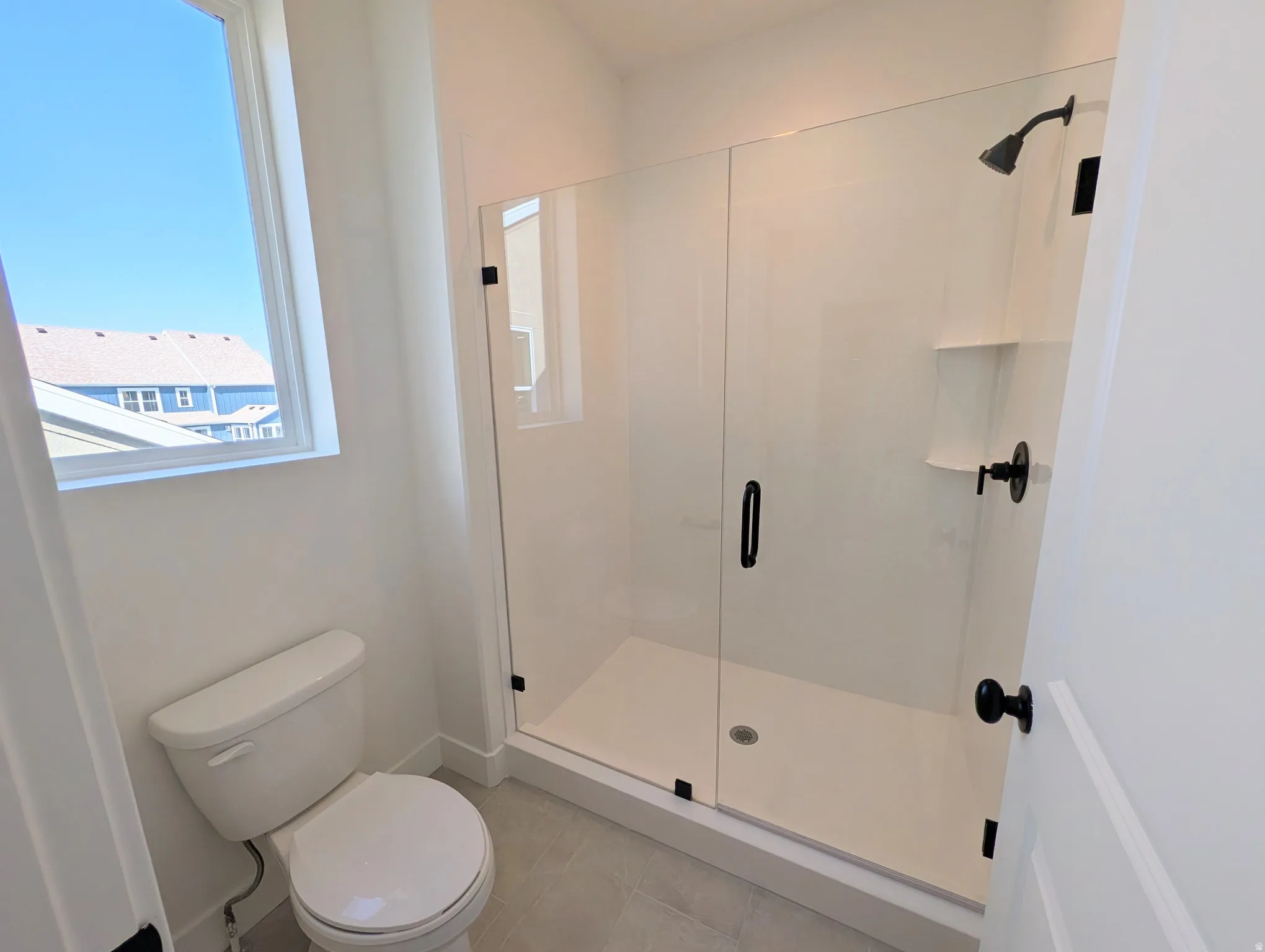 Shower enclosure with clear glass door, matte black hardware, and an integrated shelf