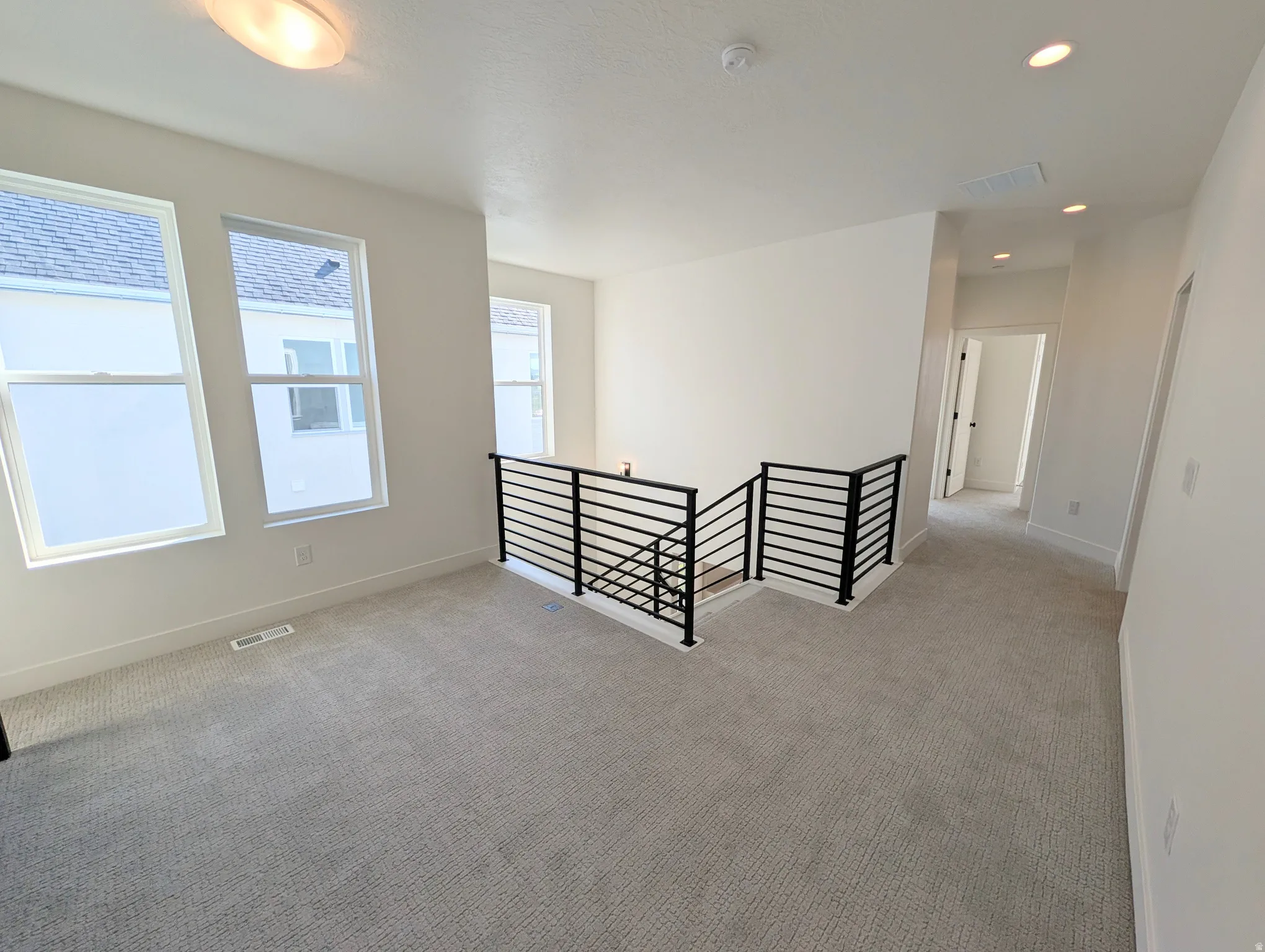Upper-level landing featuring textured carpet, multiple windows, a modern black metal railing, and recessed ceiling lighting
