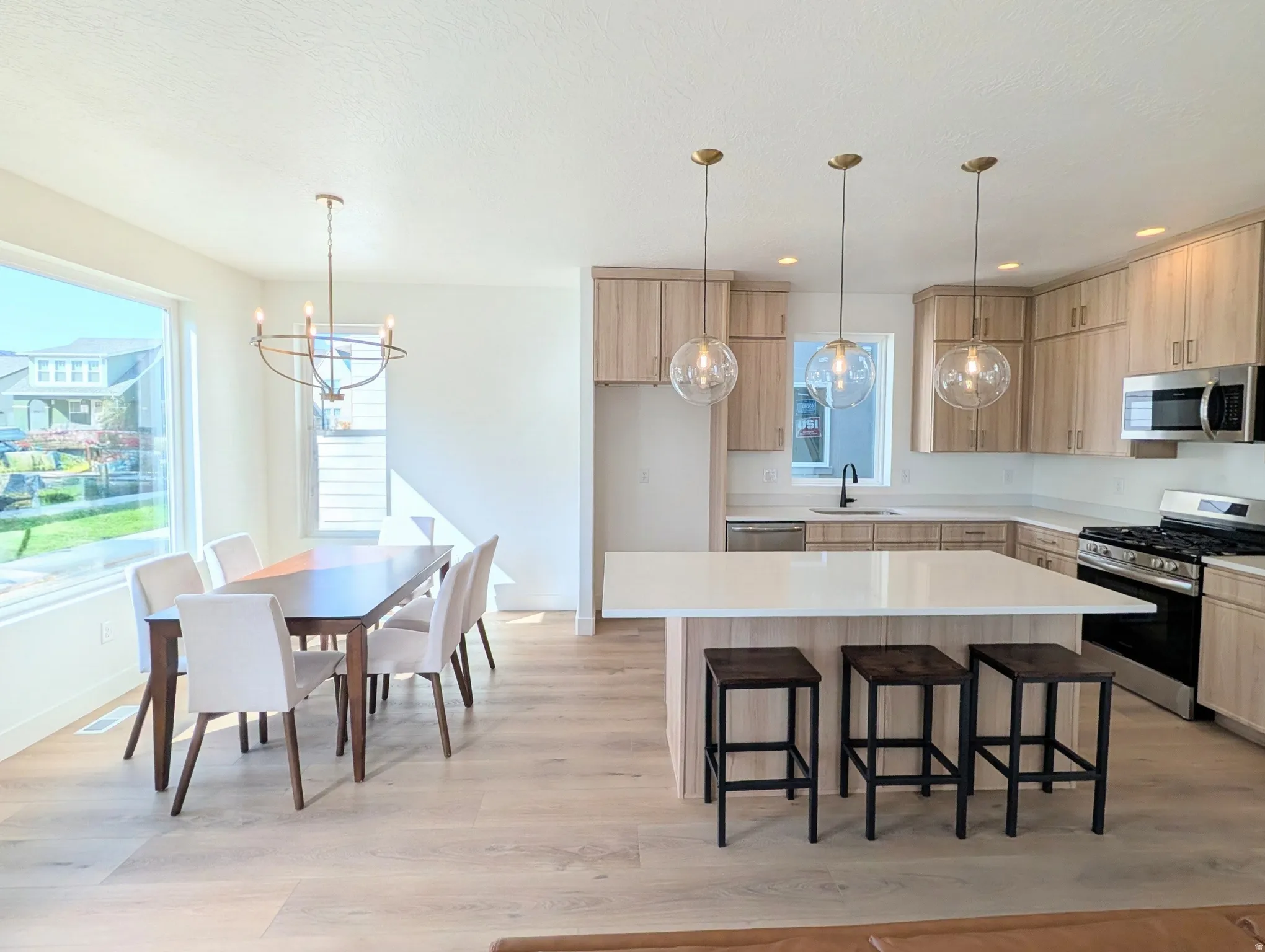 Open-concept living area featuring wood-finish flooring, a contemporary kitchen island with a light-toned countertop, and stainless steel appliances