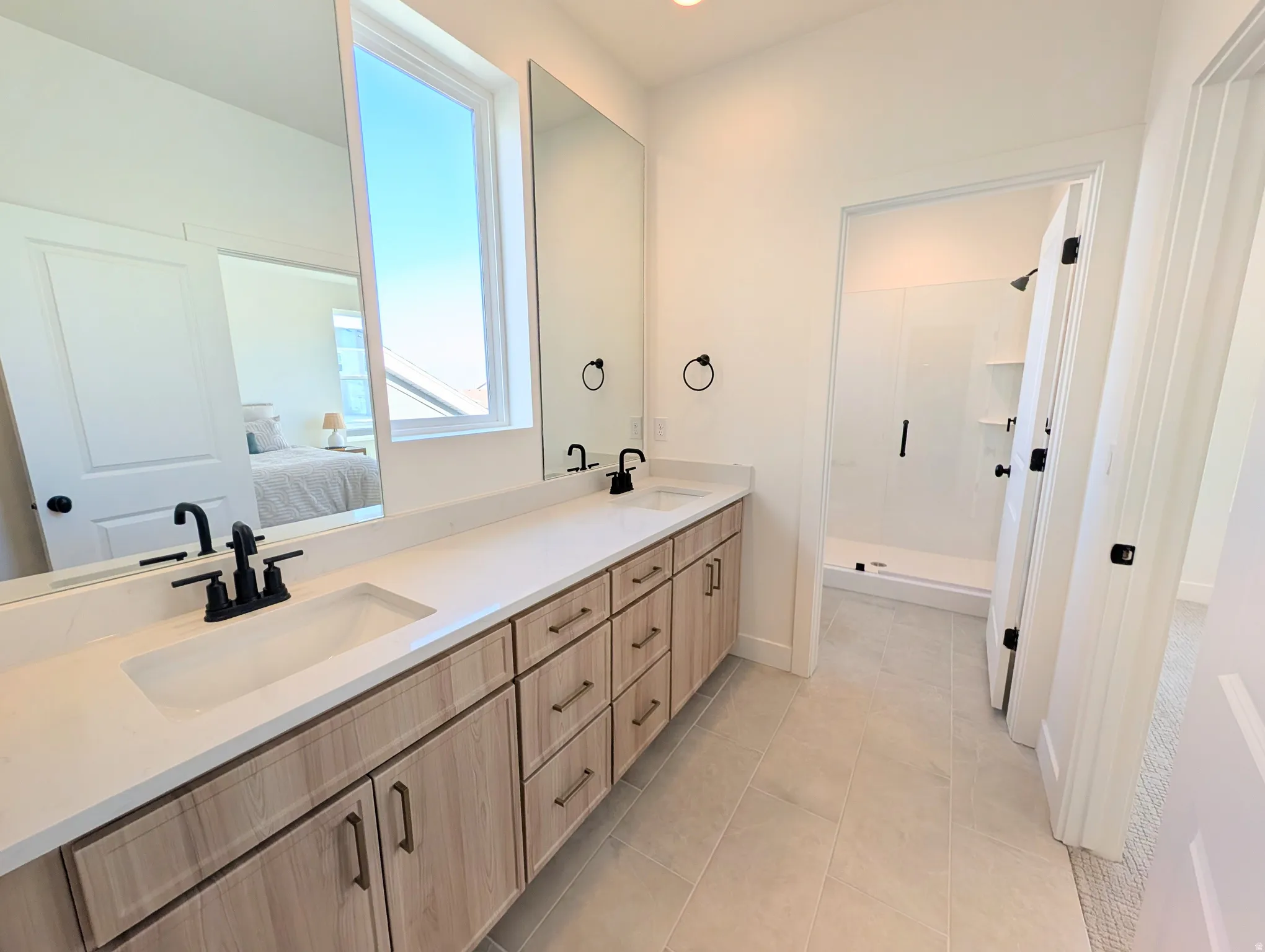 Dual vanity with undermount sinks, light wood-finish cabinetry, and matte black fixtures