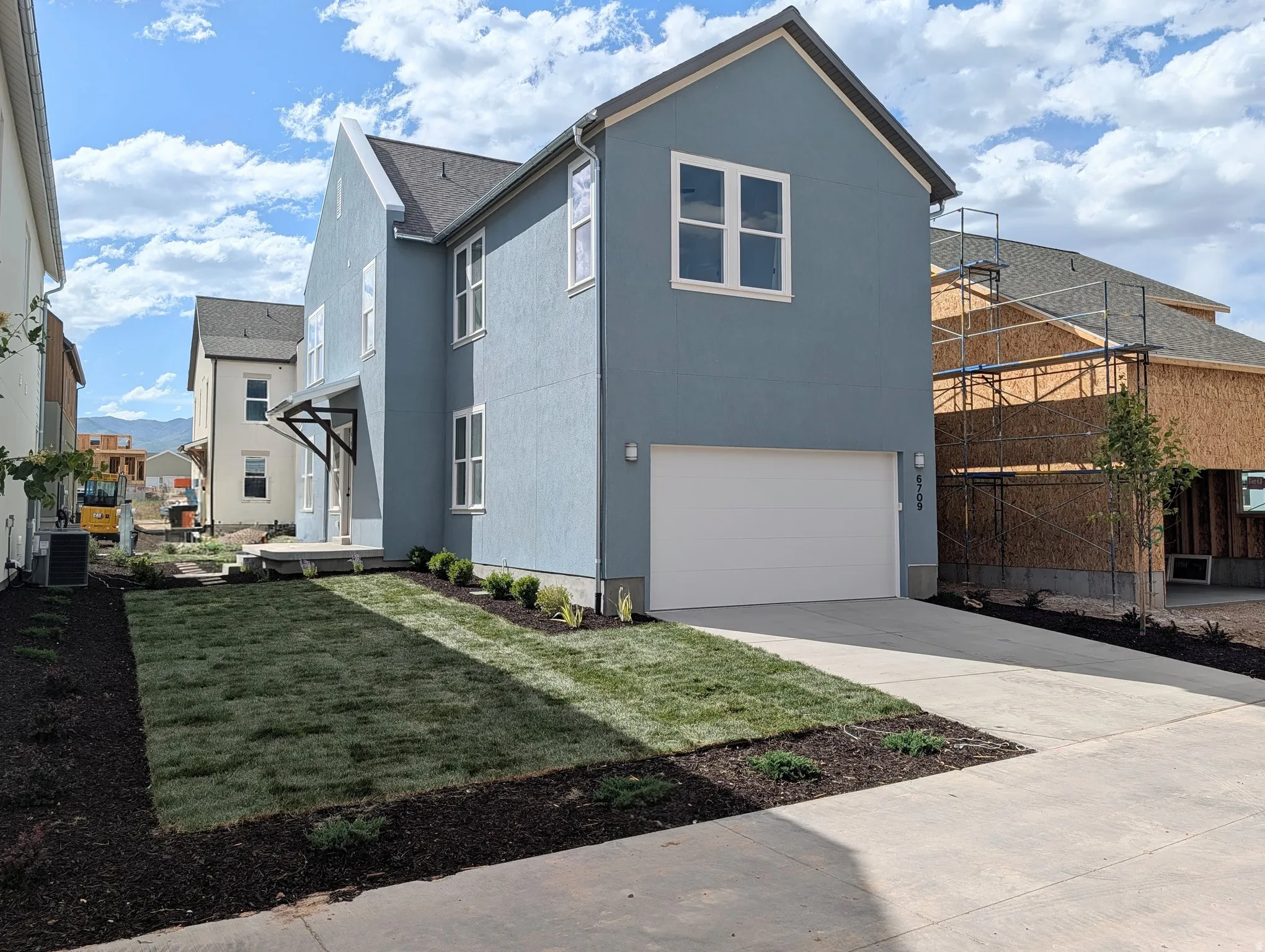 Contemporary blue-gray stucco exterior featuring a white garage door, dark soffits, and a landscaped front yard with newly installed sod