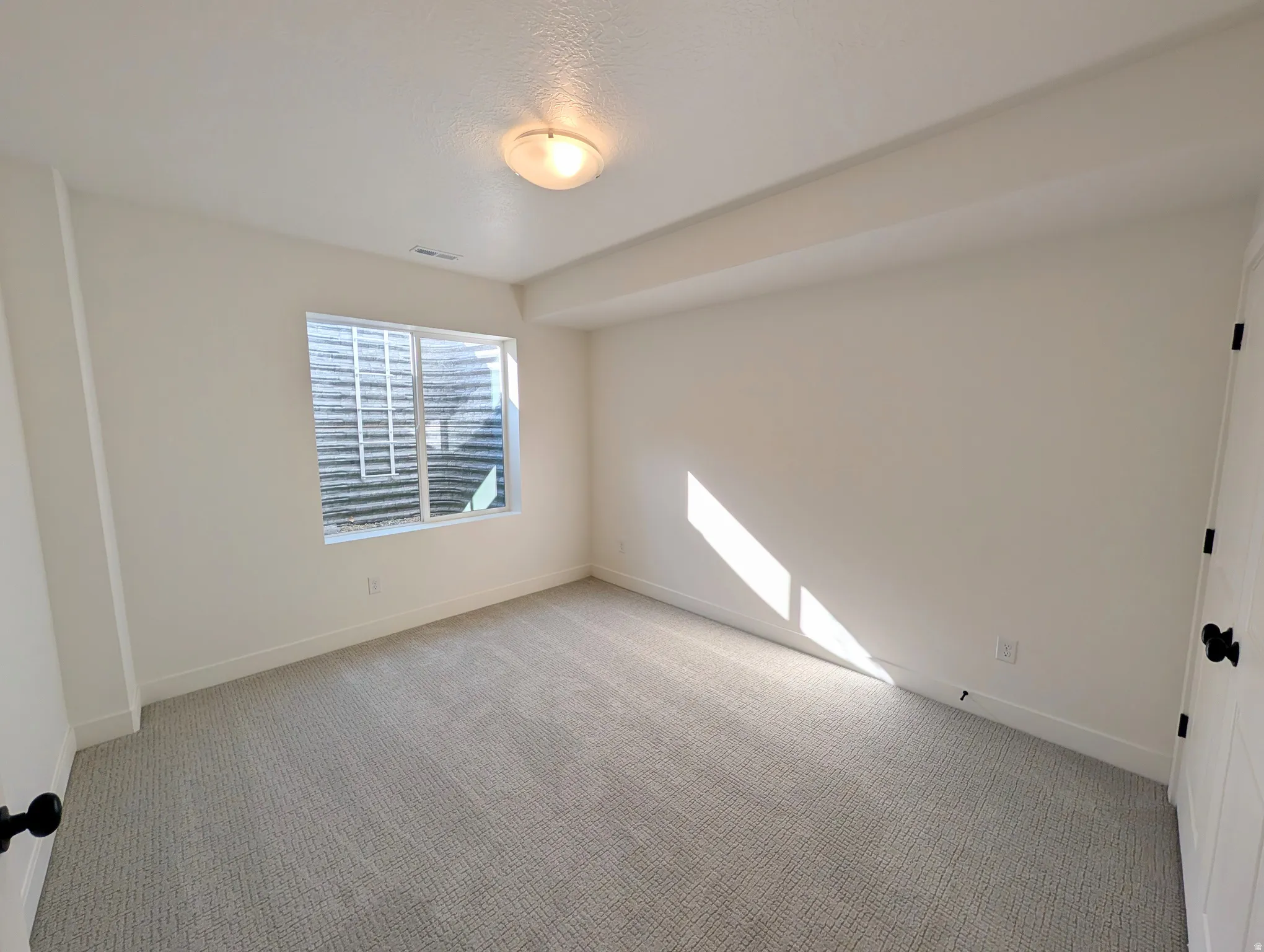 Neutral tone wall paint, light-colored patterned carpeting, flush mount ceiling light fixture, white trim, and a window with a window well