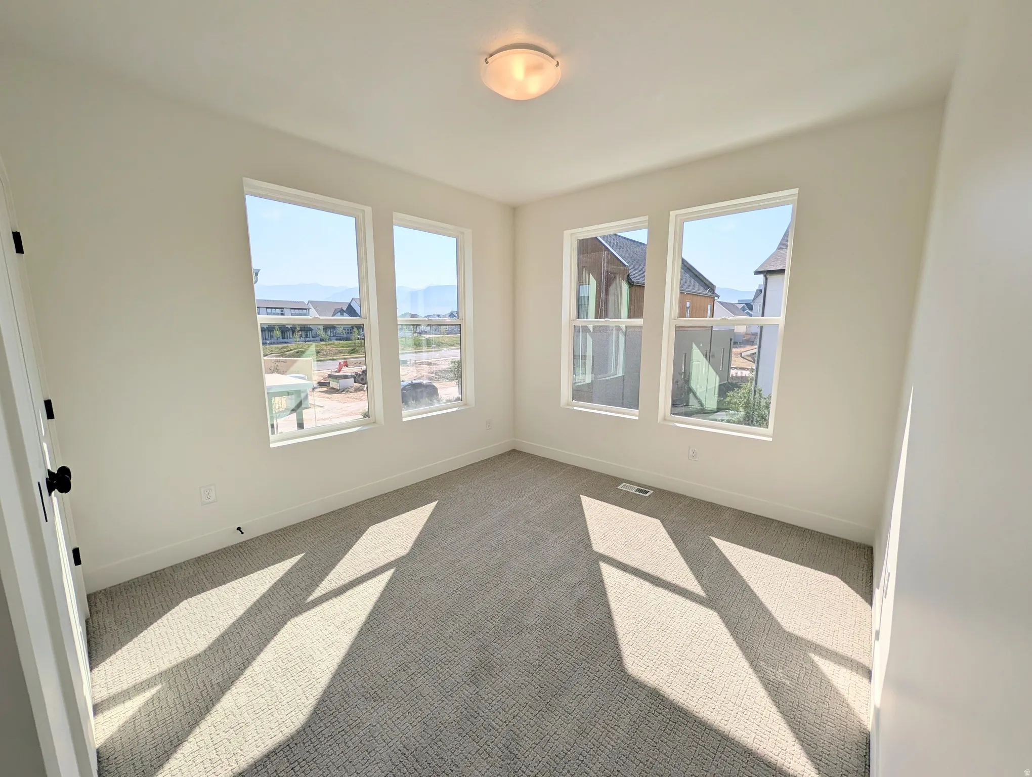 Light-filled room featuring five large windows, neutral-toned carpet, and a ceiling-mounted light fixture