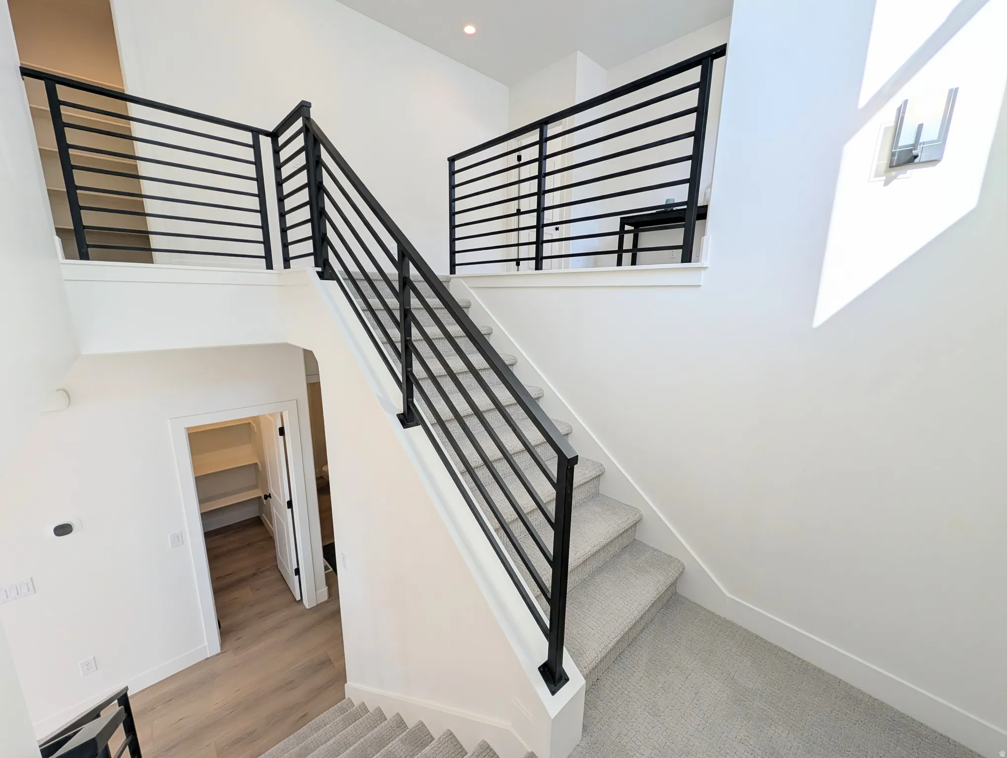 Multi-level interior featuring modern horizontal black railings, light gray carpeted stairs, recessed lighting, and wood-finish flooring