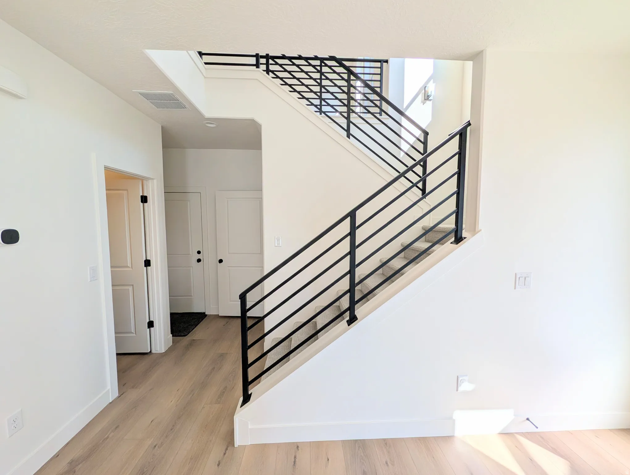 Modern staircase with black metal railing and light wood-finish flooring