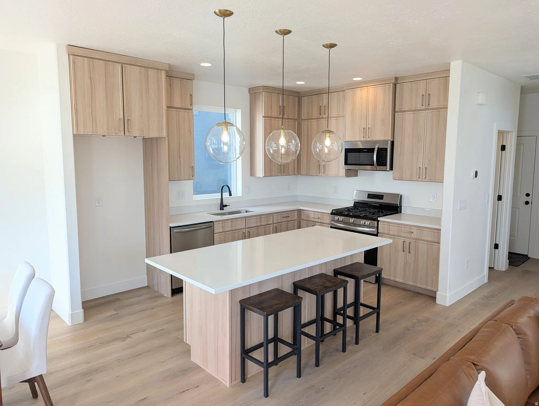 Kitchen featuring light wood-finish cabinetry, stainless steel appliances, a white quartz island with seating, pendant lighting, and wood-finish flooring