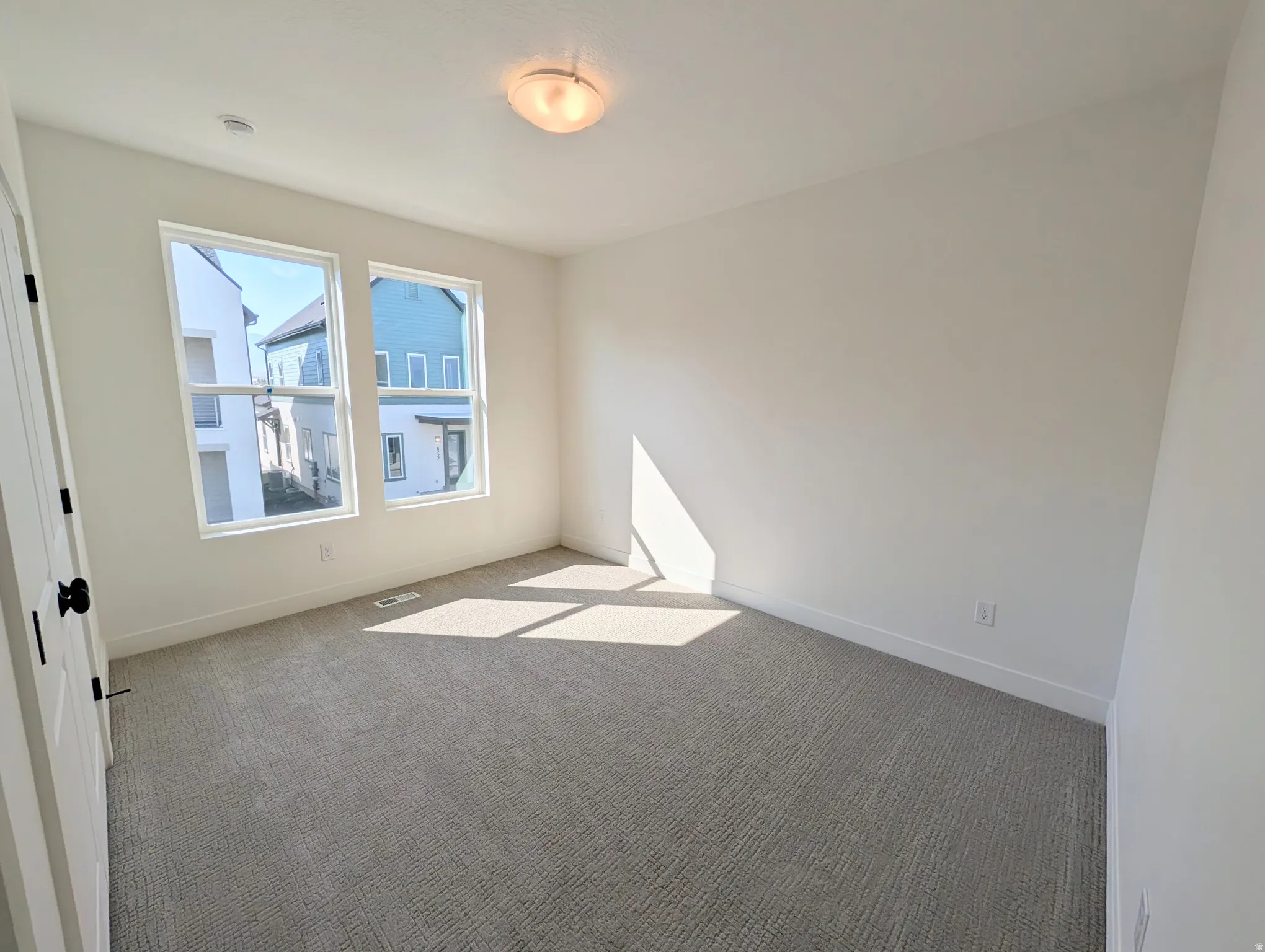Neutral wall paint, two large windows, flush mount ceiling light, and textured carpet flooring